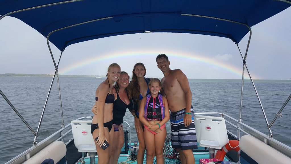 Dolphin swim tour boat with family on board and a rainbow behind them.